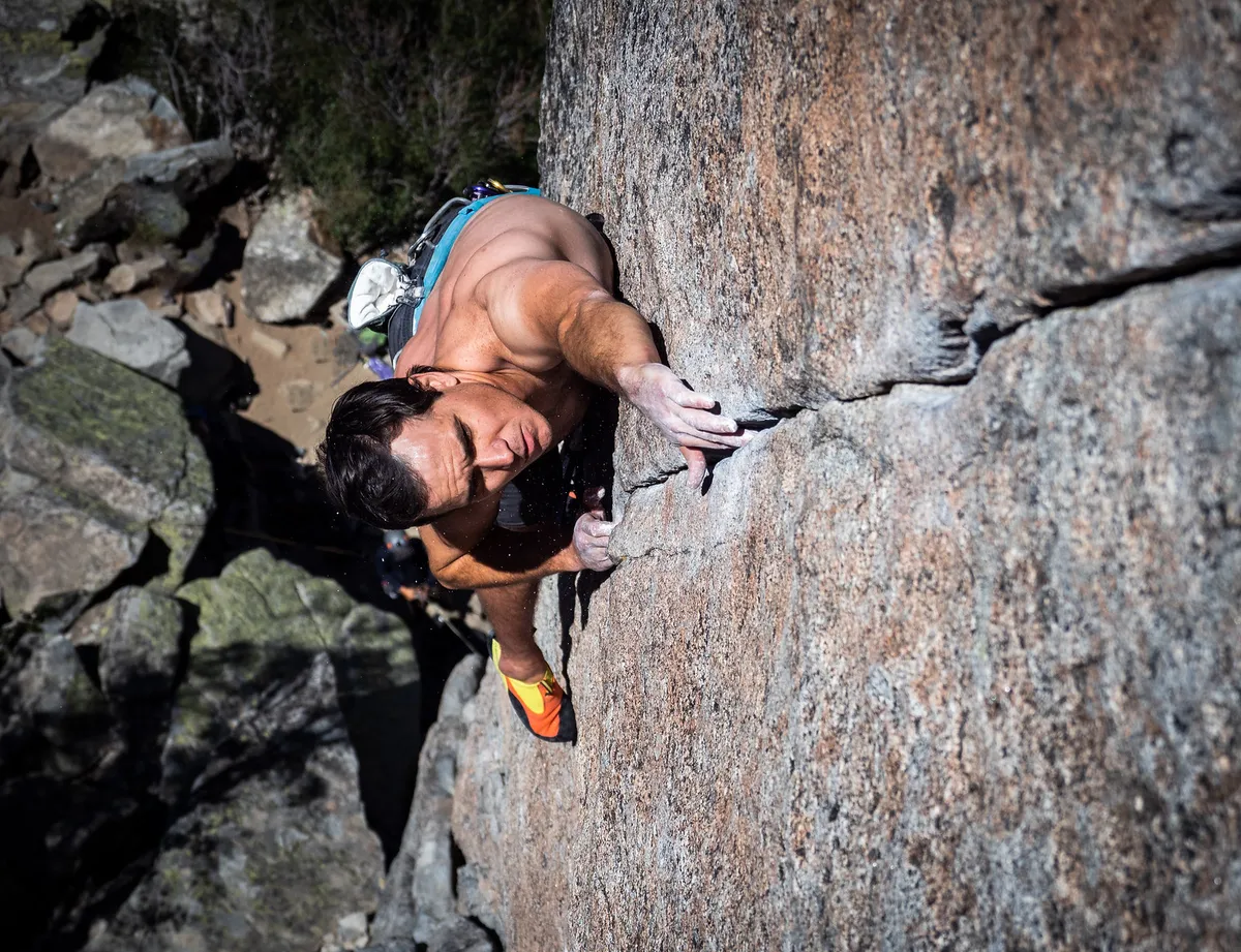 Looking down on a shirtless climber reaching up a granite crack