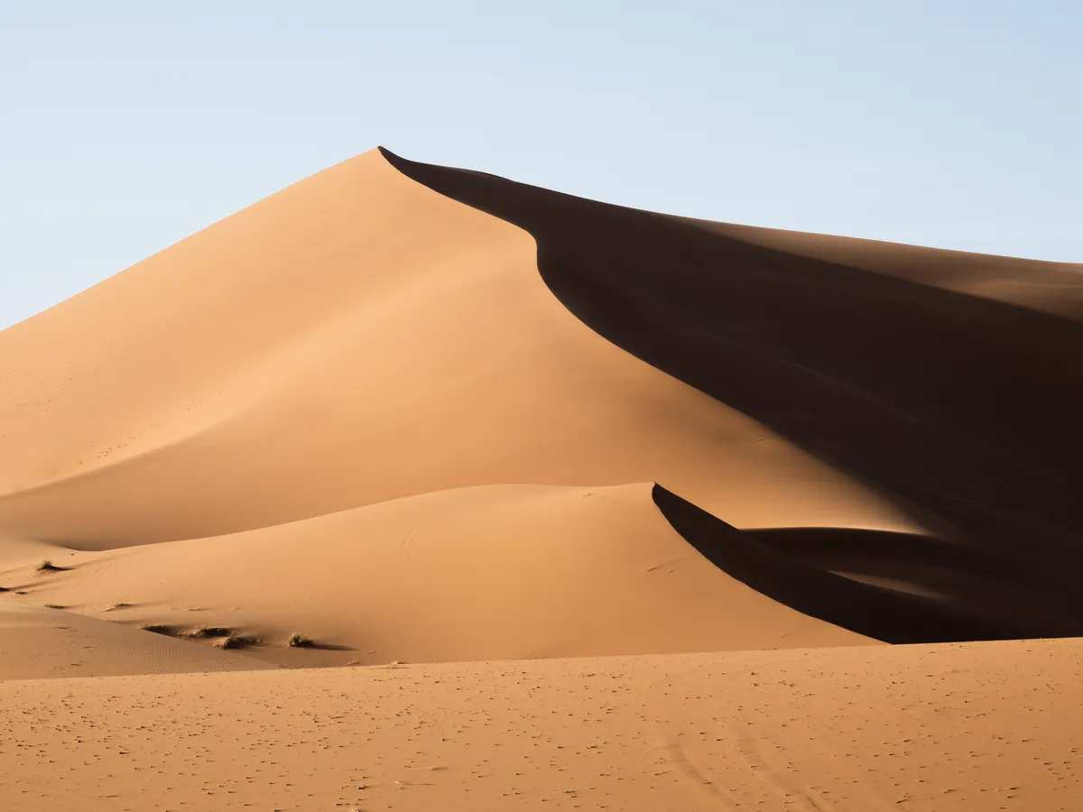 A single sharp-crested sand dune, half in shadow, under a pale sky