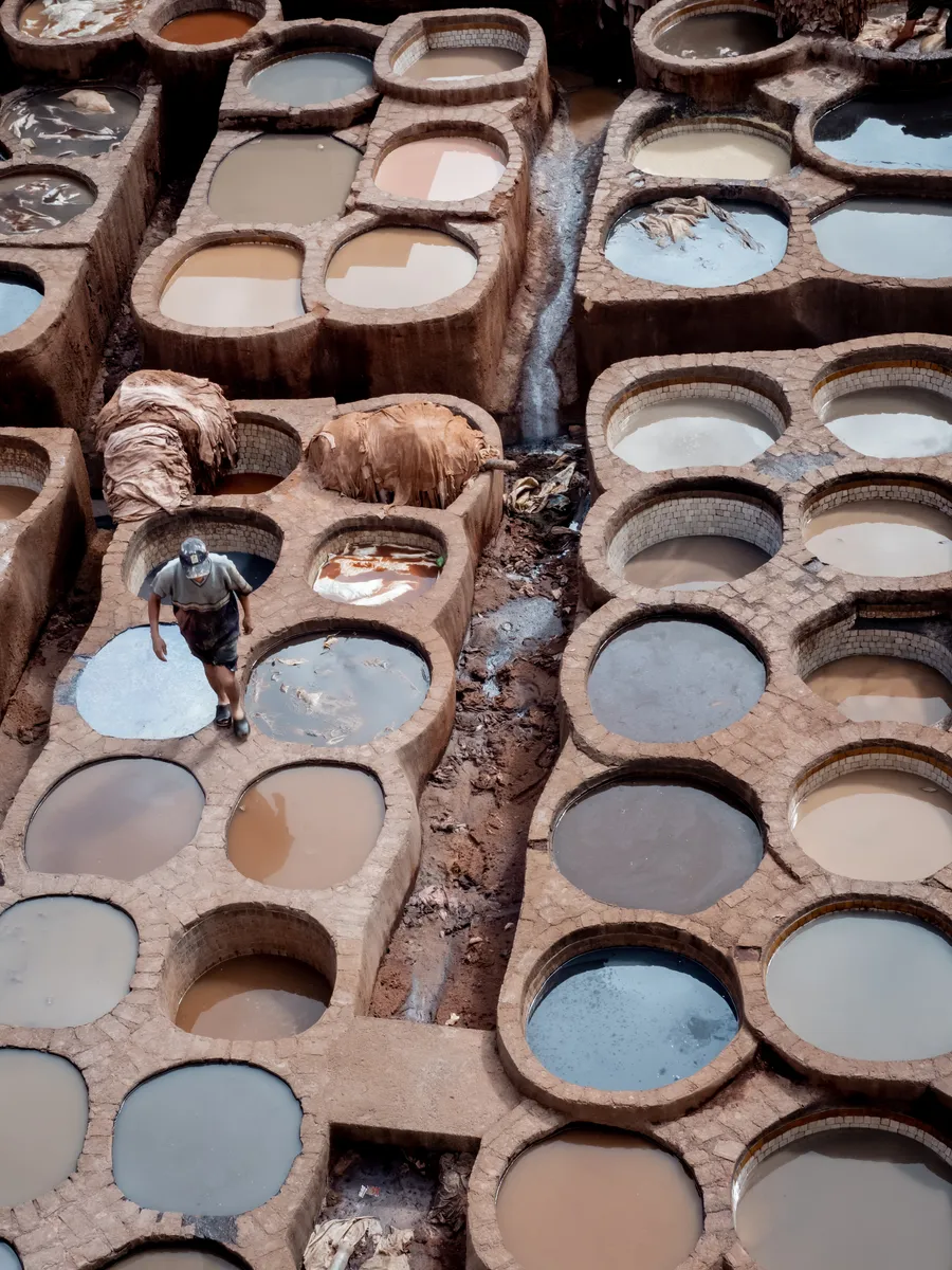 Looking down on round stone dye pits at a leather tannery, a worker crossing between them